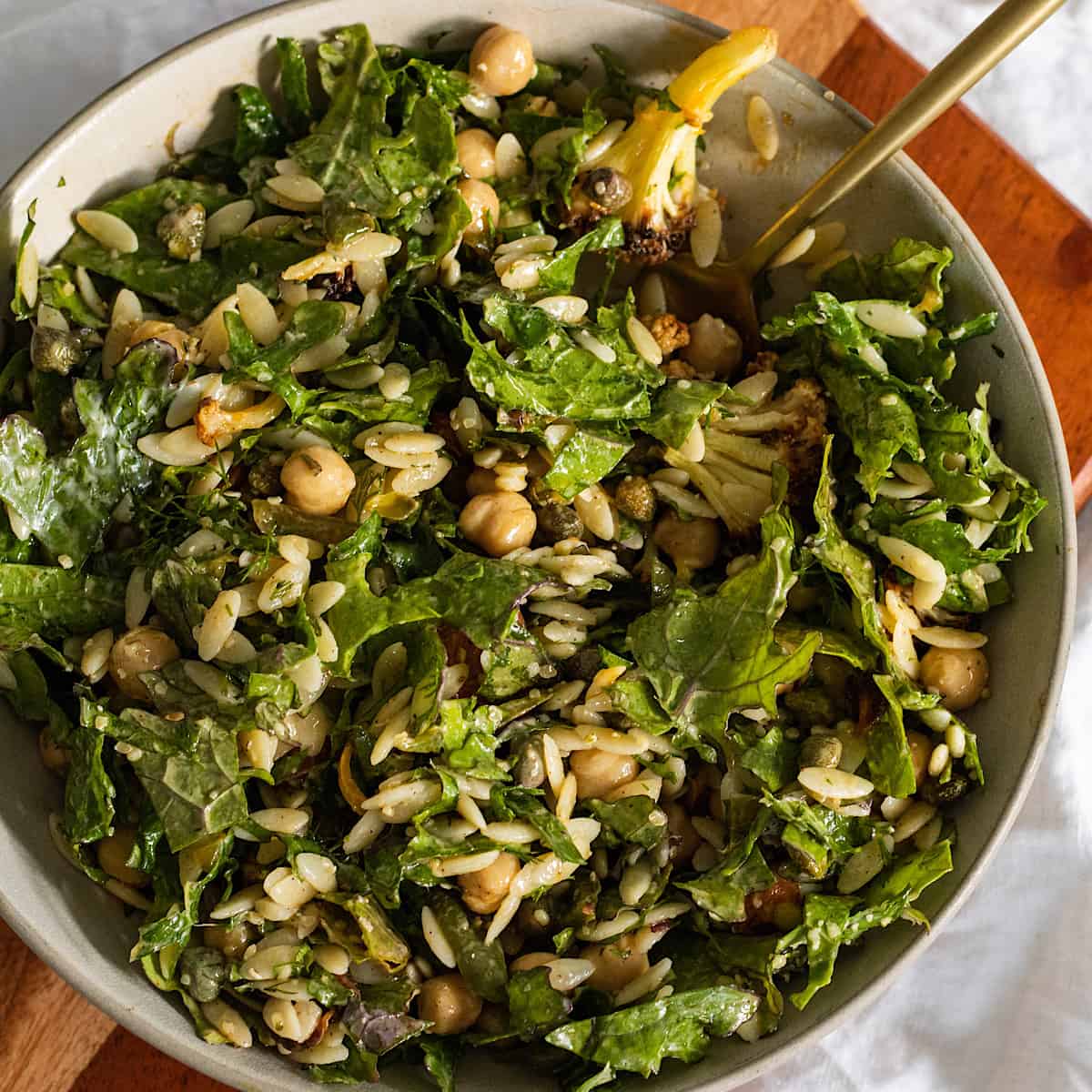 Overhead view of kale salad with chickpeas and orzo on a plate with a golden spoon on the side.