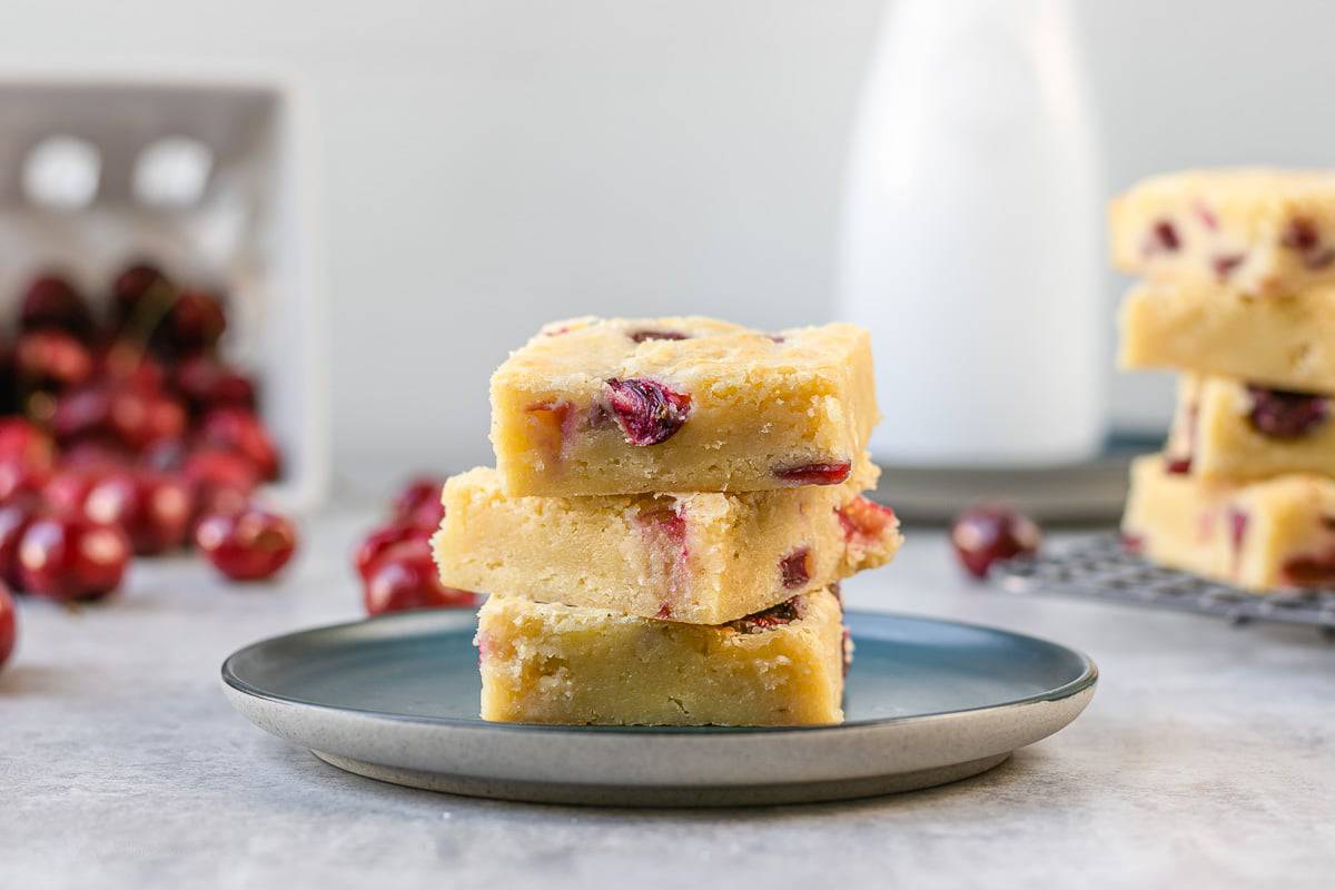 Side angle view of cherry white chocolate blondies on a blue plate.
