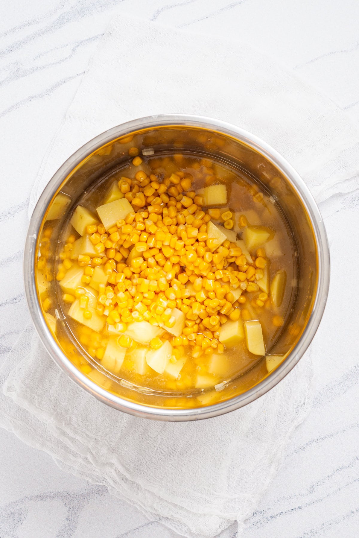 An overhead image of vegetable broth, diced potatoes, sweetcorn, salt and pepper added to an instant pot.