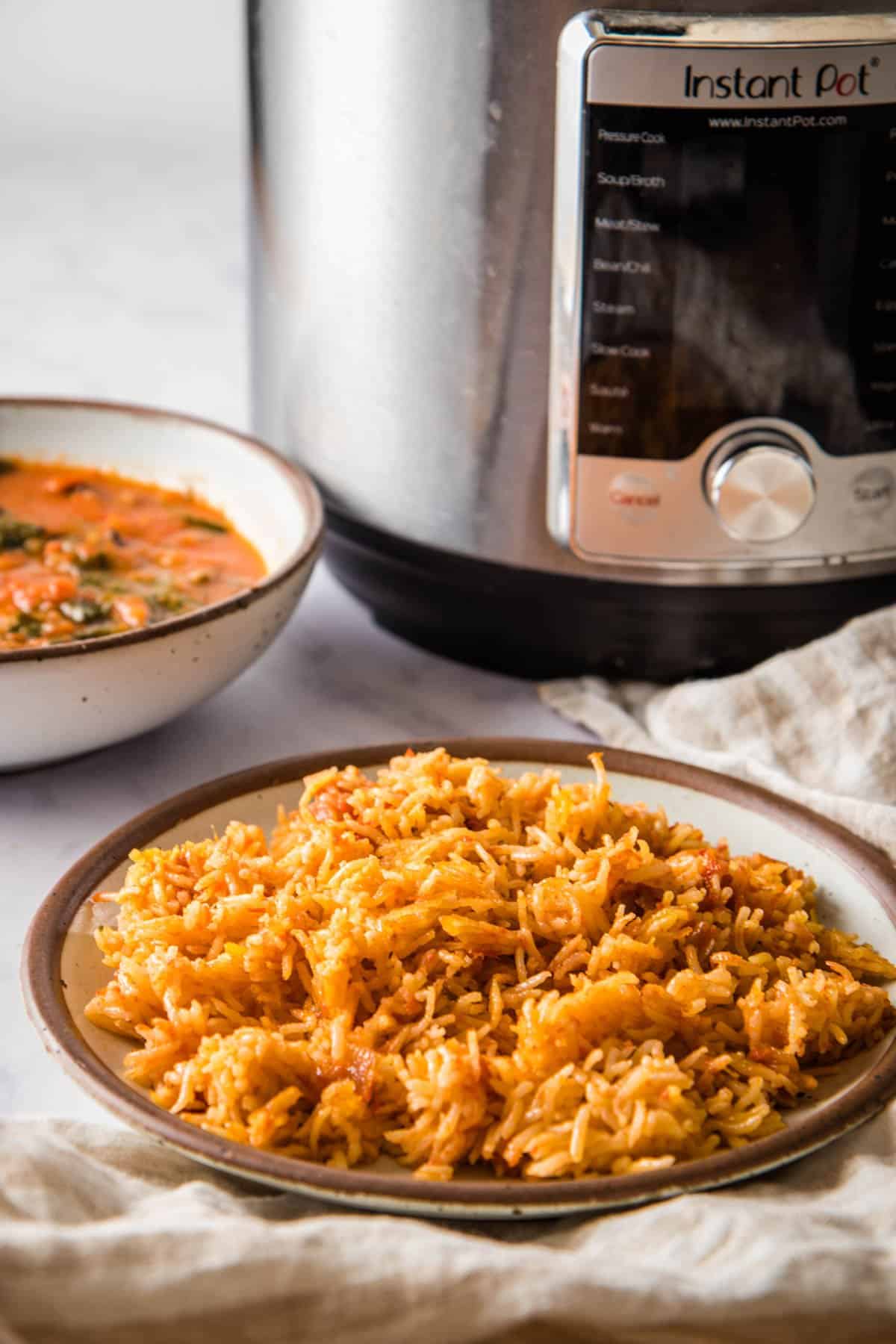 Bowl of Jollof Rice with Instant Pot and a bowl of a stew in the background