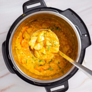 Overhead view of an instant pot full of mulligatawny soup with a ladle scooping out the dish. 