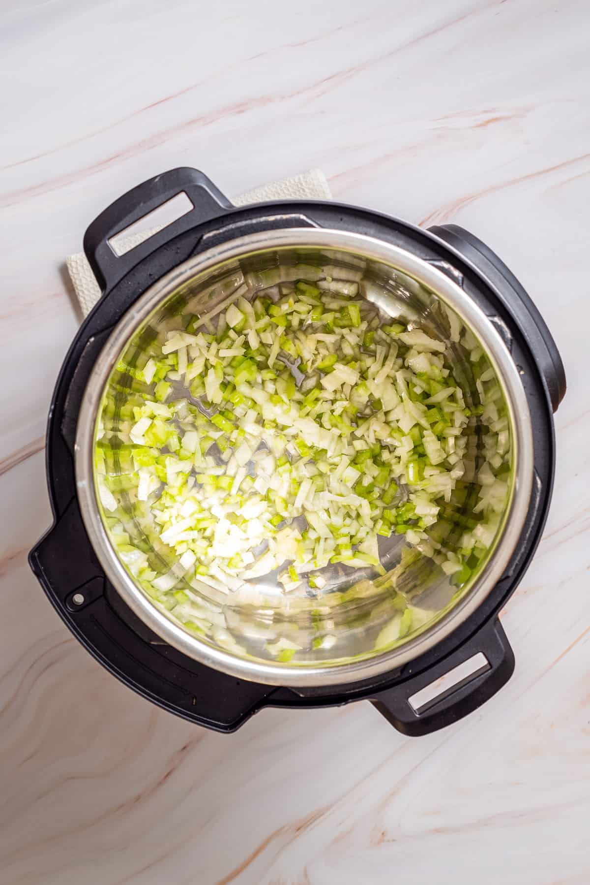 Overhead view of an instant pot with oil, onion, and celery.