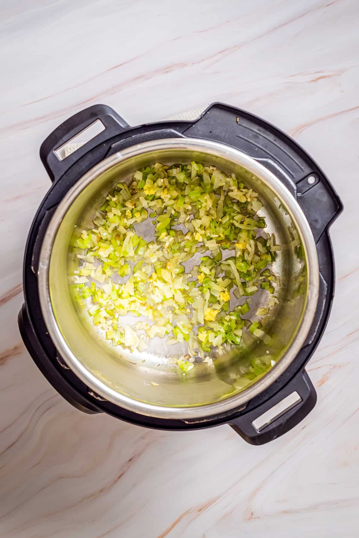 Overhead view of cooked onion and celery in an instant pot added with garlic and ginger.