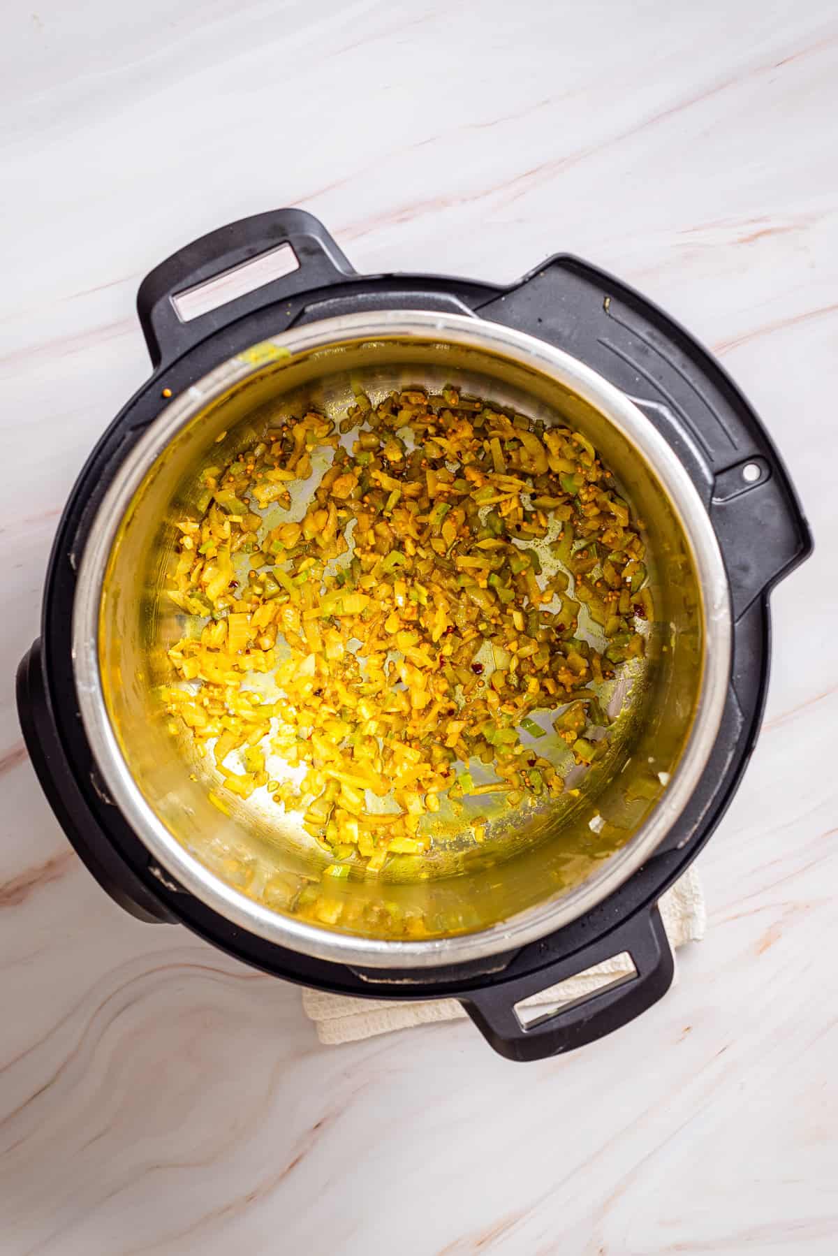 Overhead view of mixed celery, onion, garlic, and ginger added with mustard seeds, turmeric, curry powder, red pepper flakes, and ground cumin inside an instant pot.