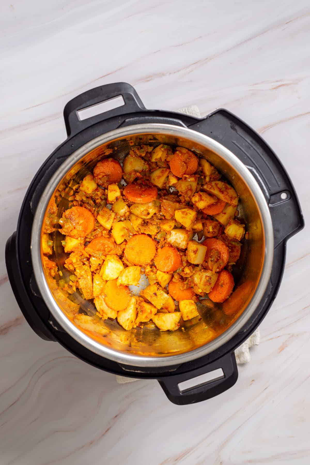 Overhead view of an instant pot with mixed celery, carrots, potatoes, spices, and apple cubes added with tomato paste and flour.