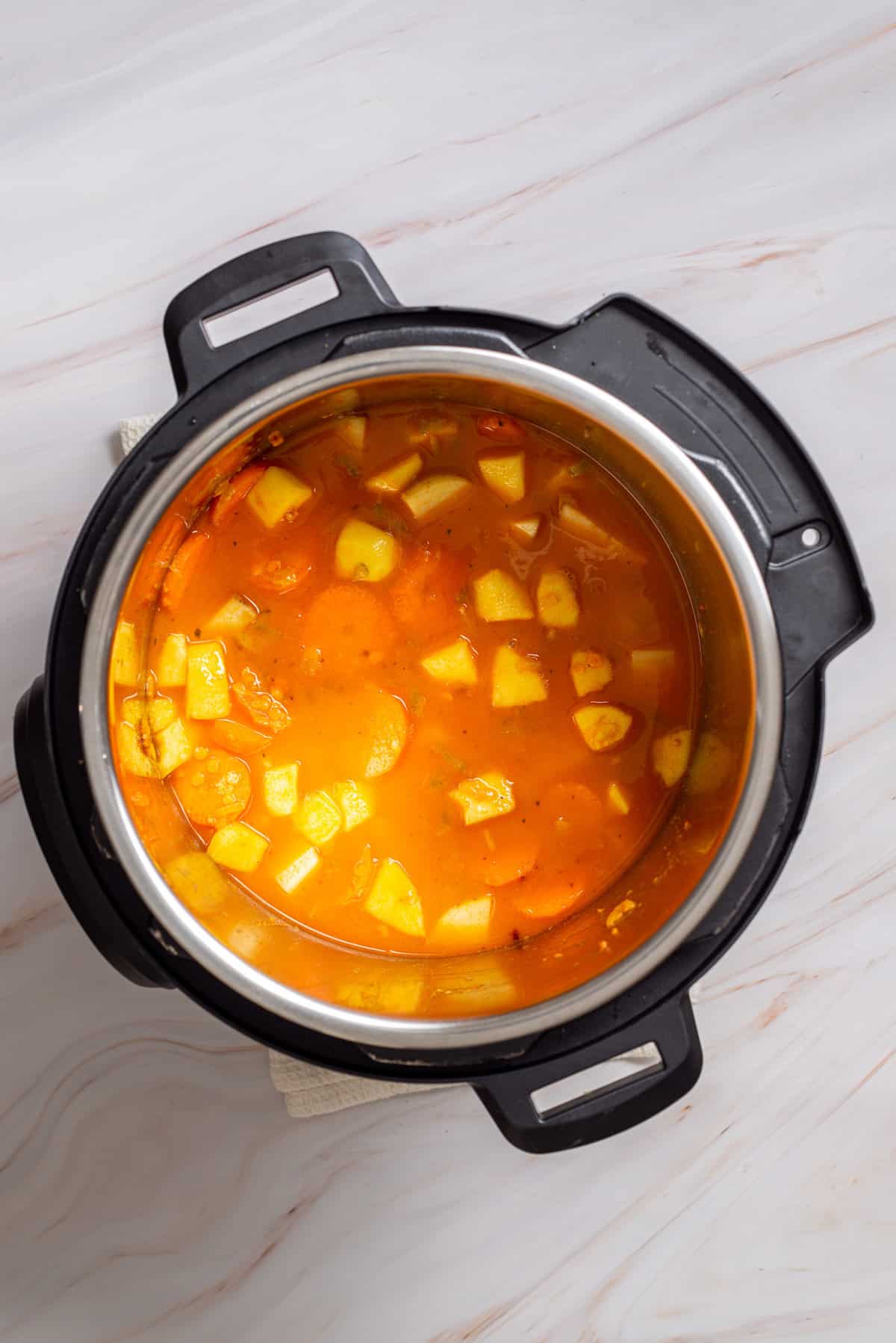 Overhead view of an instant pot with mixed celery, carrots, potatoes, spices, apple cubes, tomato paste, and flour added with masoor dal and vegetable broth.