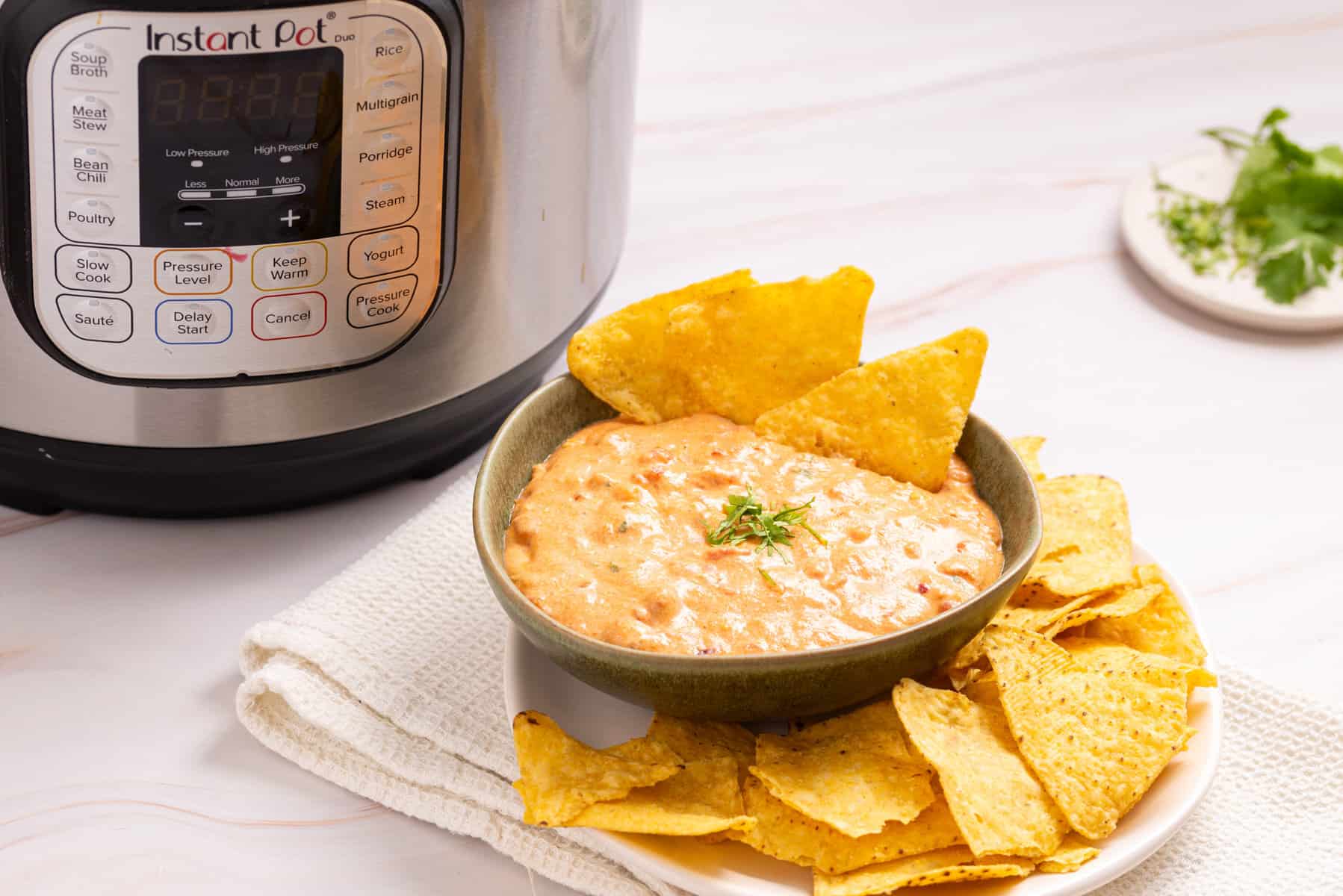 An image of queso in a bowl with nacho chips on the side and an instant pot on the back.