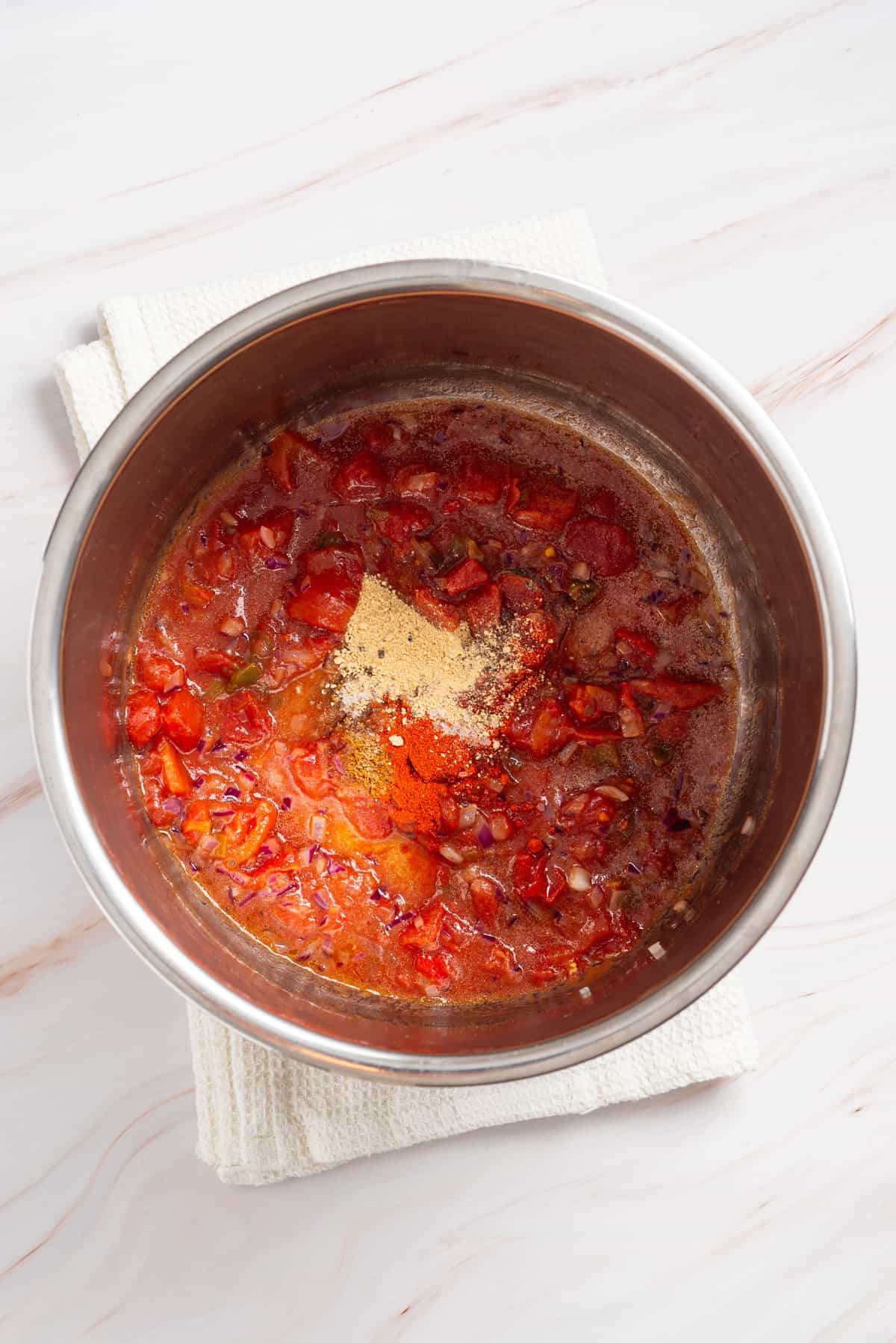 An overhead image of diced tomatoes, chili, seasonings and water in an instant pot.