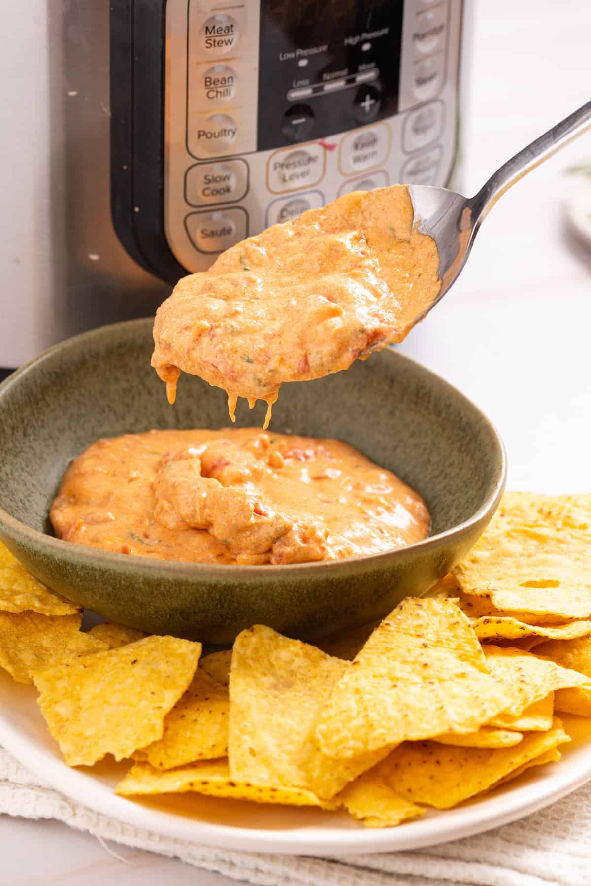 An image of a spoonful of queso dip over a bowl of instant pot queso and tortilla chips.