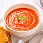 A close-up view of instant pot tomato soup placed in a white bowl with cheese toasties on the side.