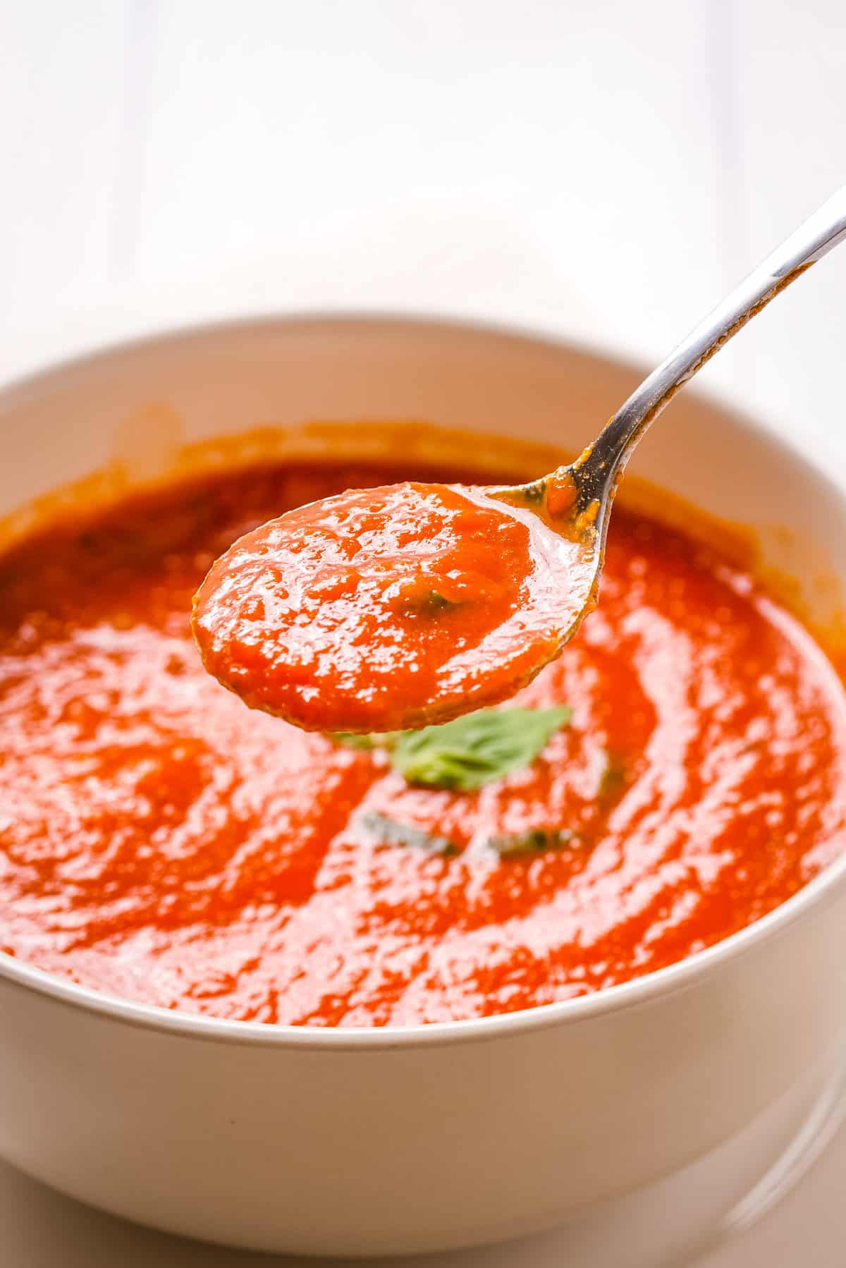 Close up shot of tomato soup in white bowl with a spoon lifting some soup out.