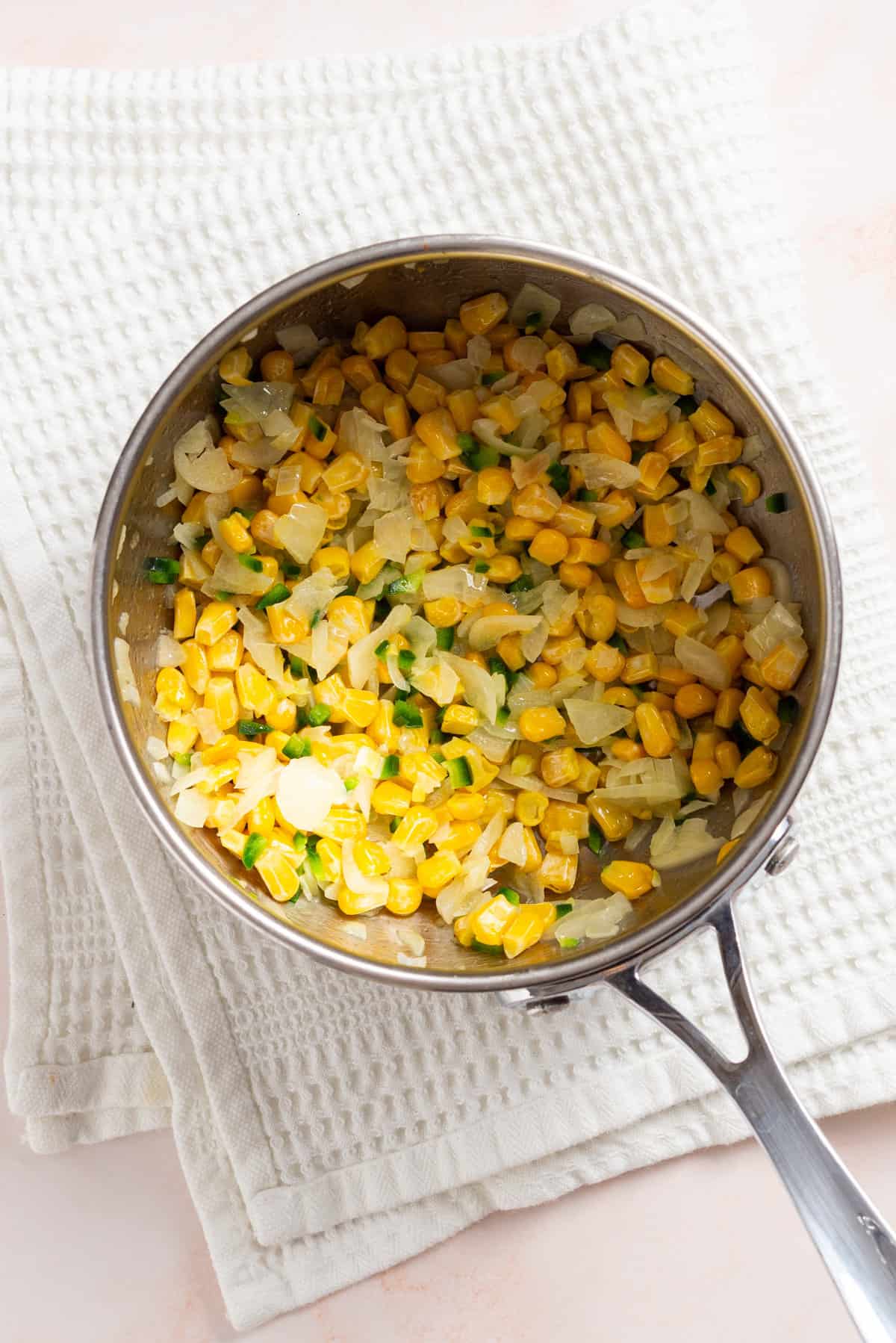 An overhead image of corn kernels added to the saucepan.