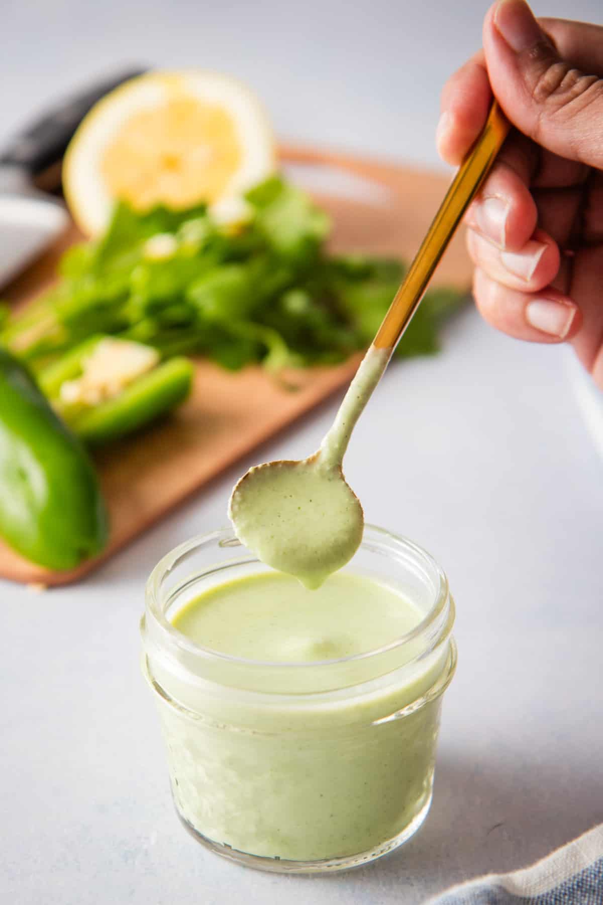 Spoonful of jalapeno ranch dressing taken out of a jar with jalapenos in the background. 