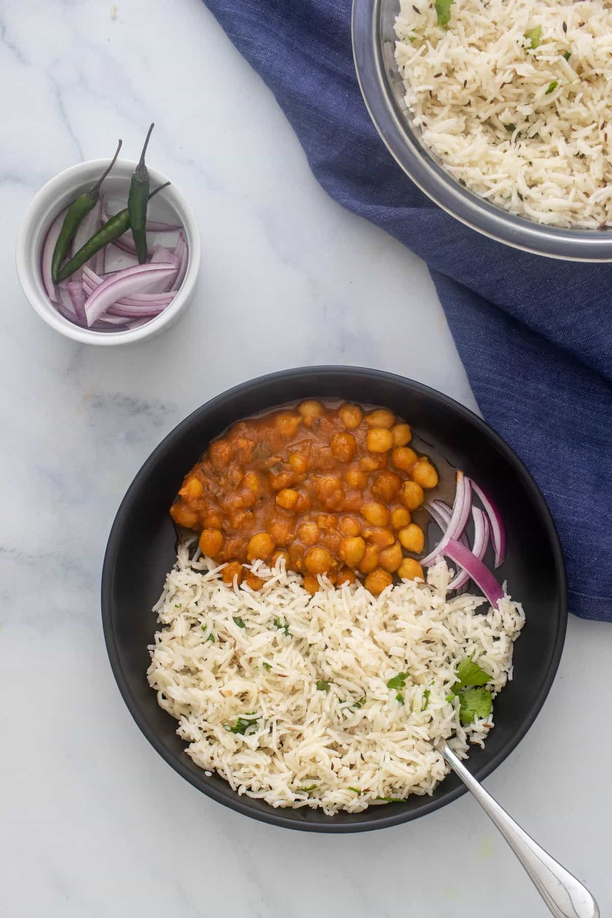 Plate of jeera rice served along with chana masala and red onions
