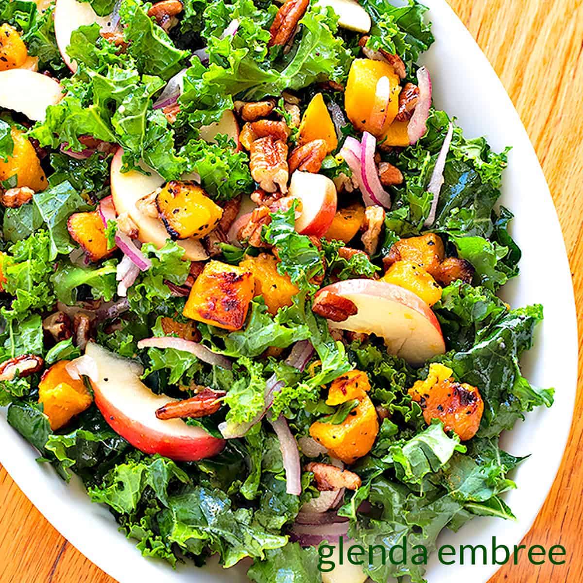 Overhead view of kale salad with apples and roastd butternut squash placed on a white plate.