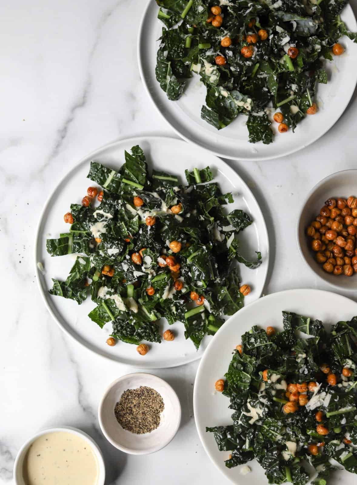 Overhead view of three white plates with kale Caesar salad with crispy chickpeas.