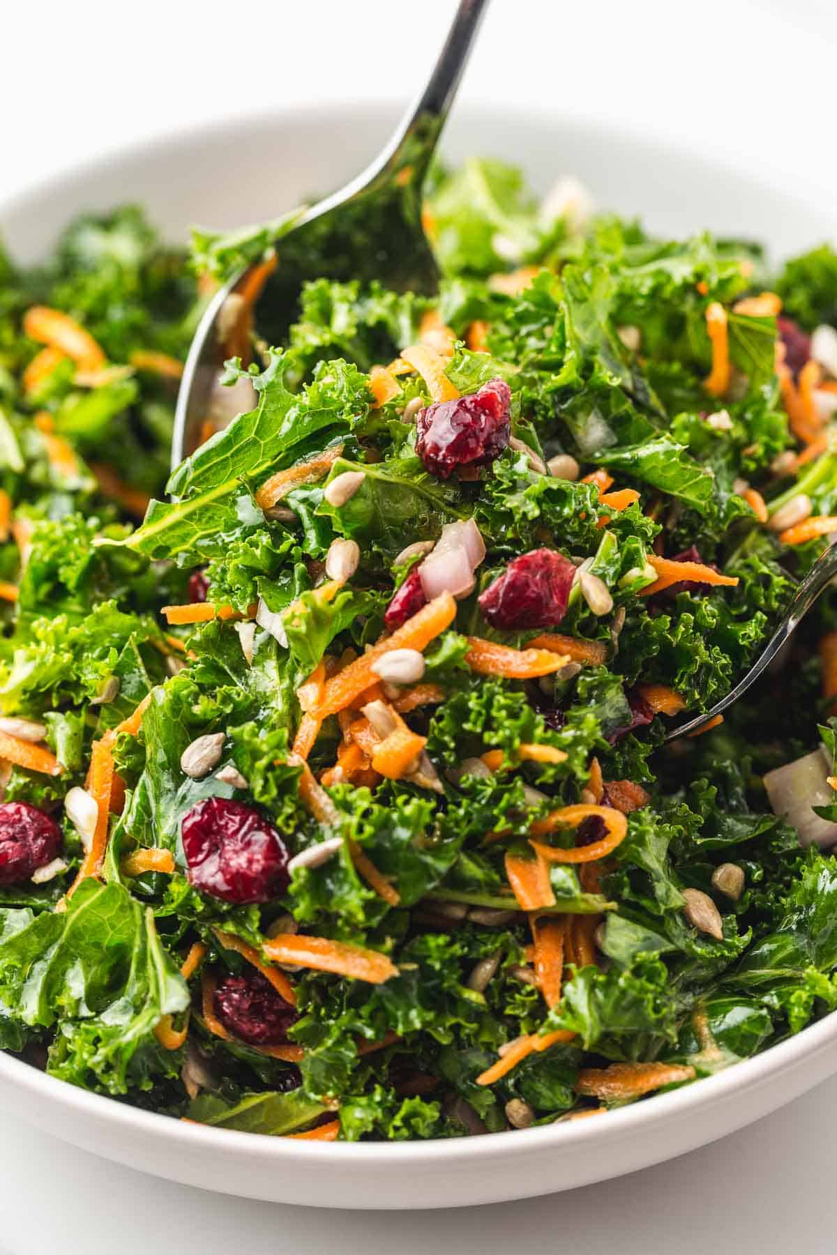Close-up view of kale salad with simple lemon vinaigrette in a white bowl with a spoon mixing the salad.