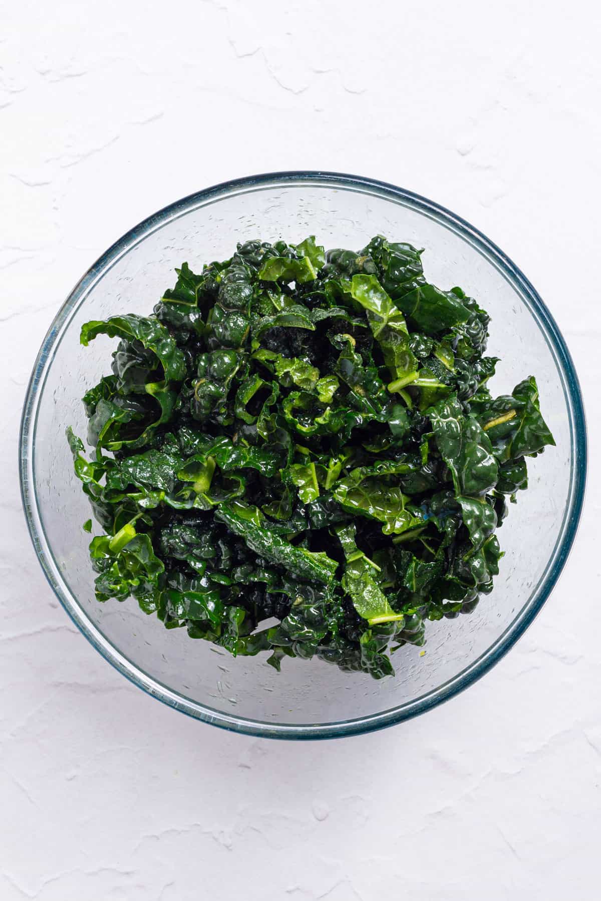 An image of kale leaves with salad dressing tossed in a bowl