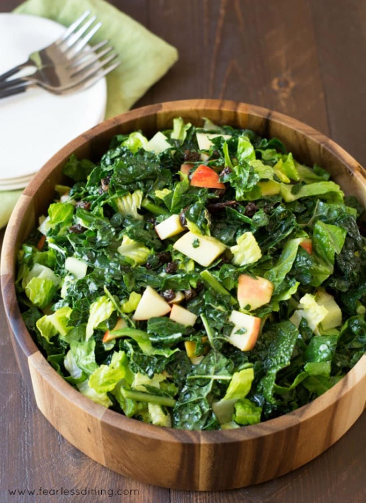 An overhead view of kid friendly kale apple salad placed on a wooden serving dish with fork next to it.
