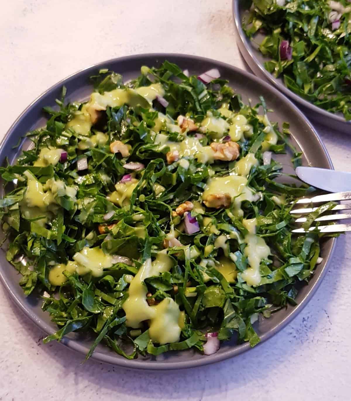 Overhead view of a plate full of kale salad with avocado dressing on top.