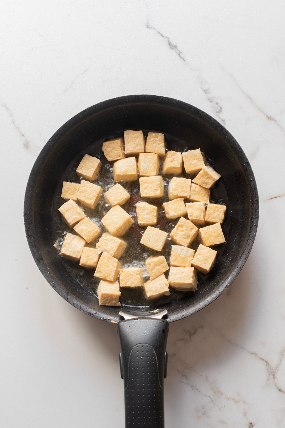 An overhead image of frying tofu cubes on a skillet.