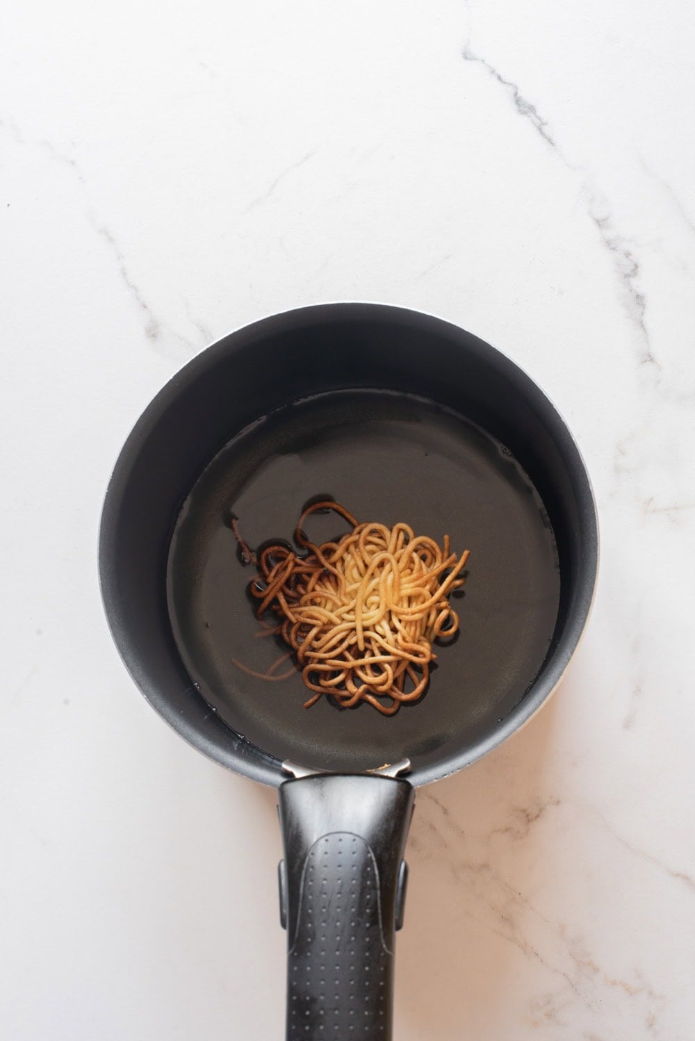 An overhead image of cooking the noodles in a pot with oil.