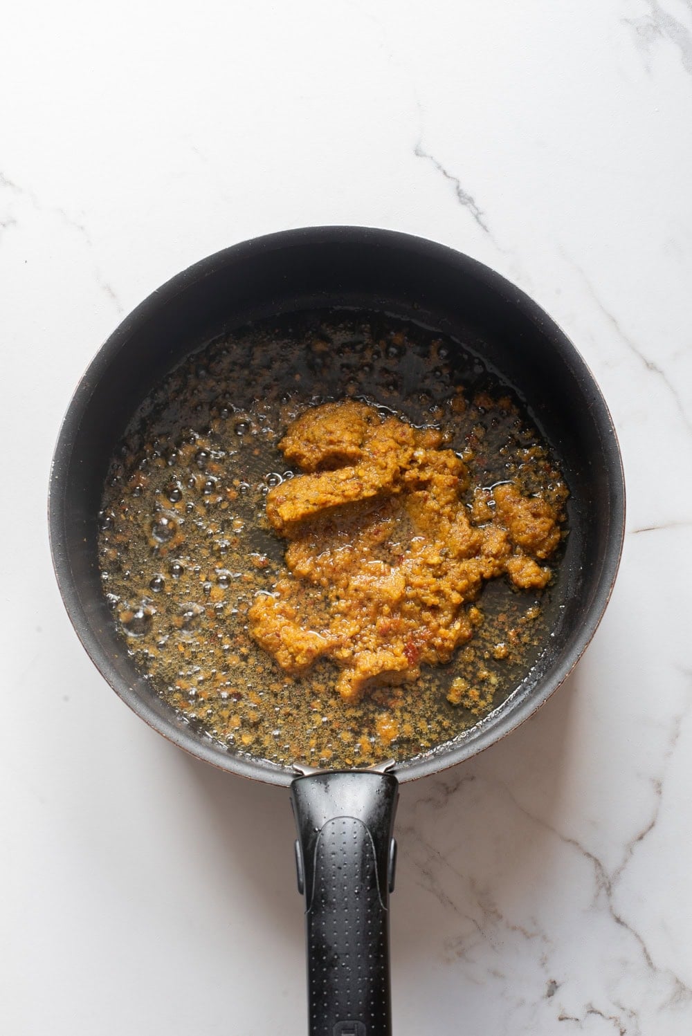 An overhead image of adding khao soi paste in a saucepan.
