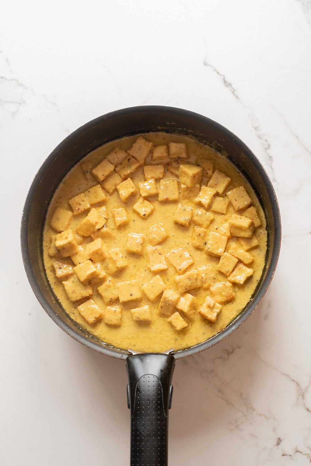 An overhead image of adding coconut cream and tofu on the saucepan.
