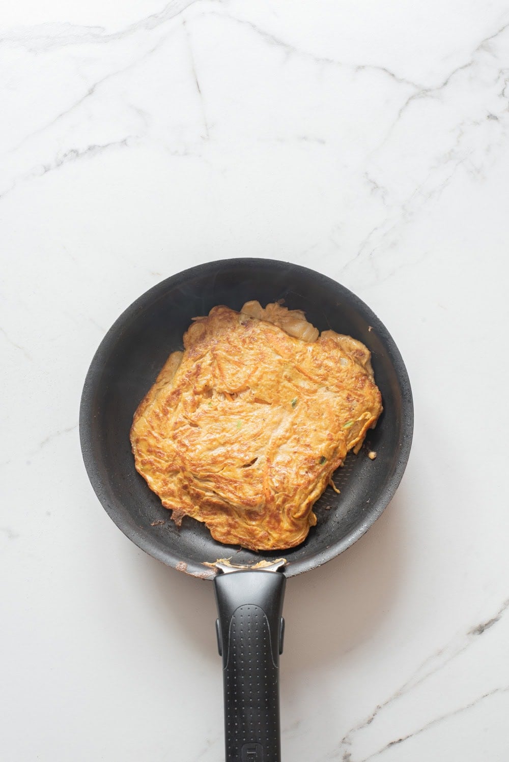 Vegetable egg omelet cooking in a skillet, shaped into a square for Korean egg sandwich.