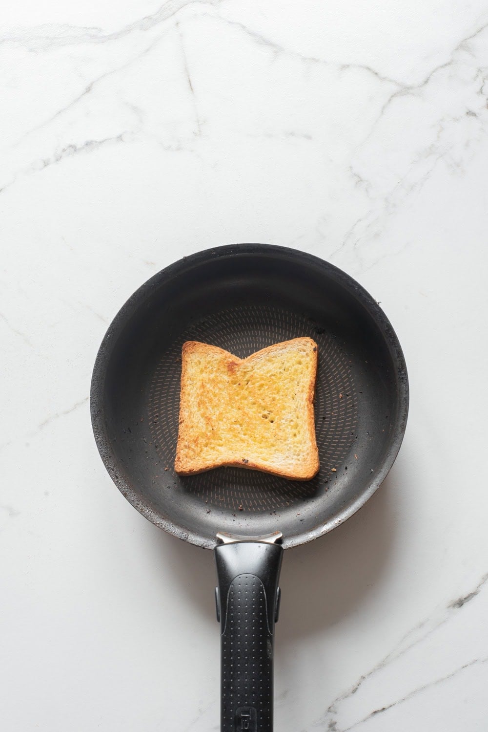 Slice of bread with butter toasting in a skillet.
