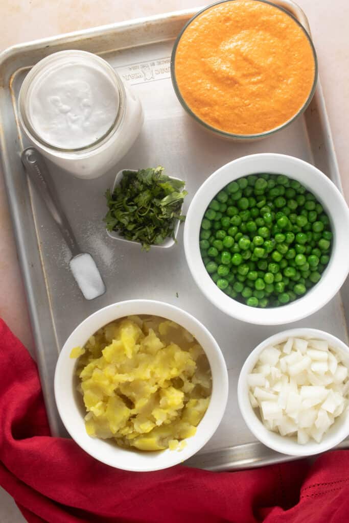 Ingredients for korma laid out on a tray - tomatoes, onions, ginger, garlic, chili peppers chili powder, and coconut pulsed together into a spice base; boiled potatoes, peas, chopped onions, coconut cream, salt and cilantro
