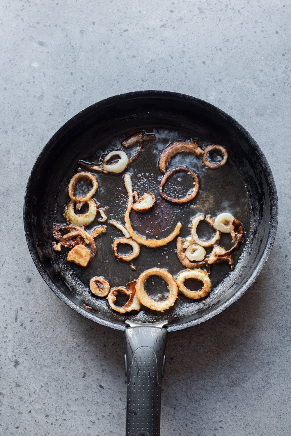 Crispy fried onion rings cooking in a skillet for koshari.