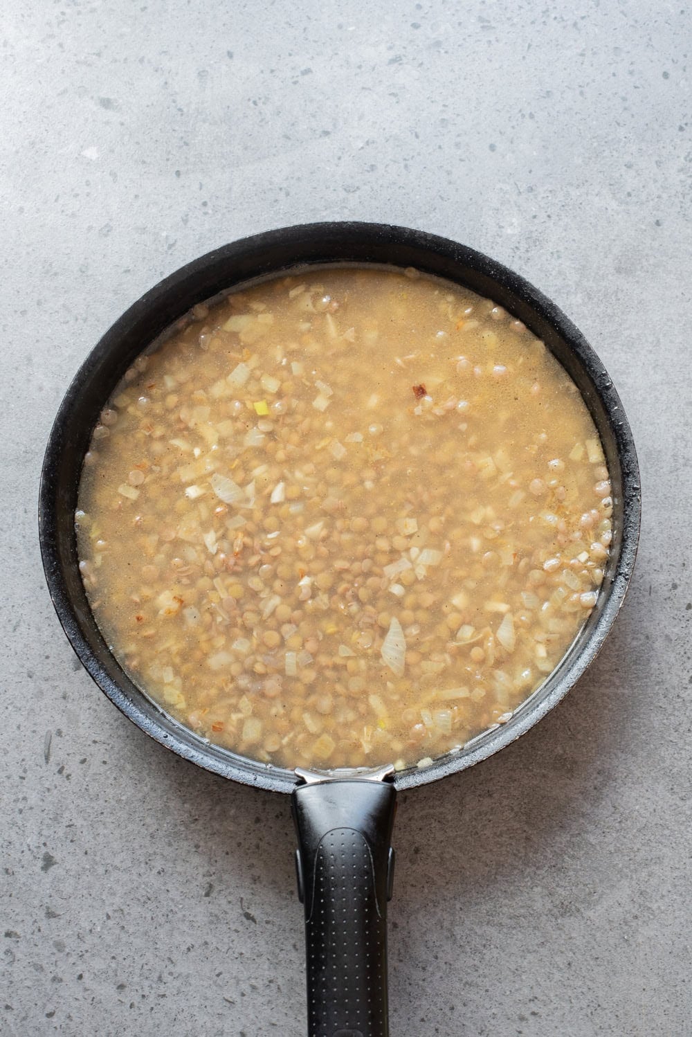 Lentils and rice cooking together in a pot with broth and spices.