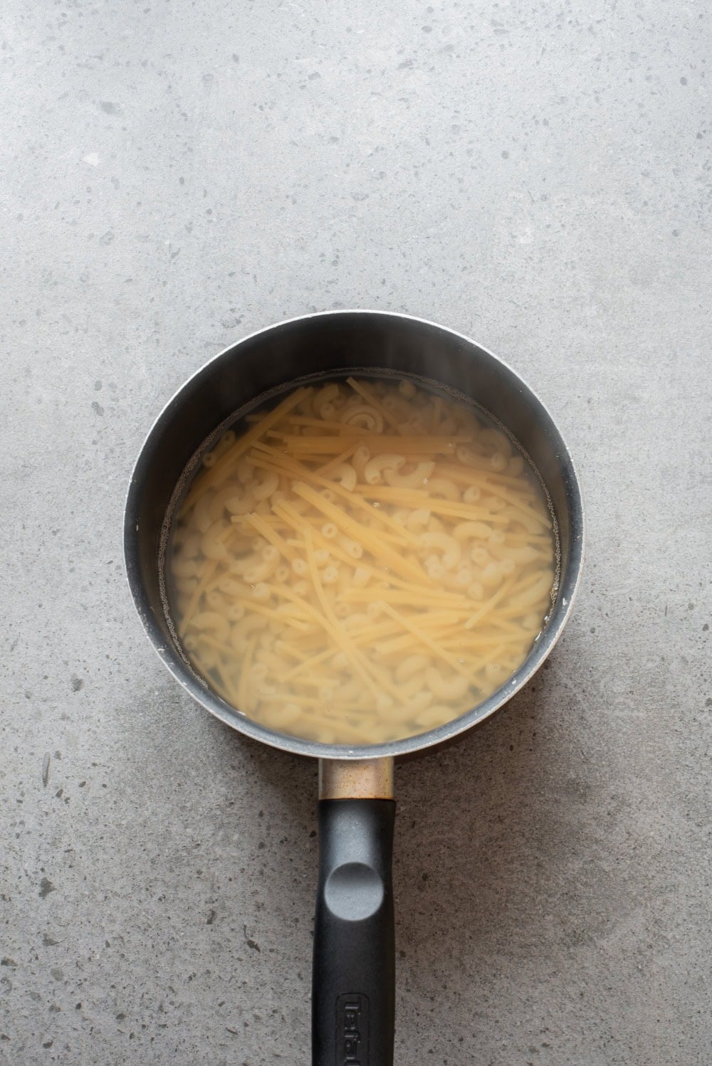 Elbow macaroni and broken spaghetti boiling in a saucepan.