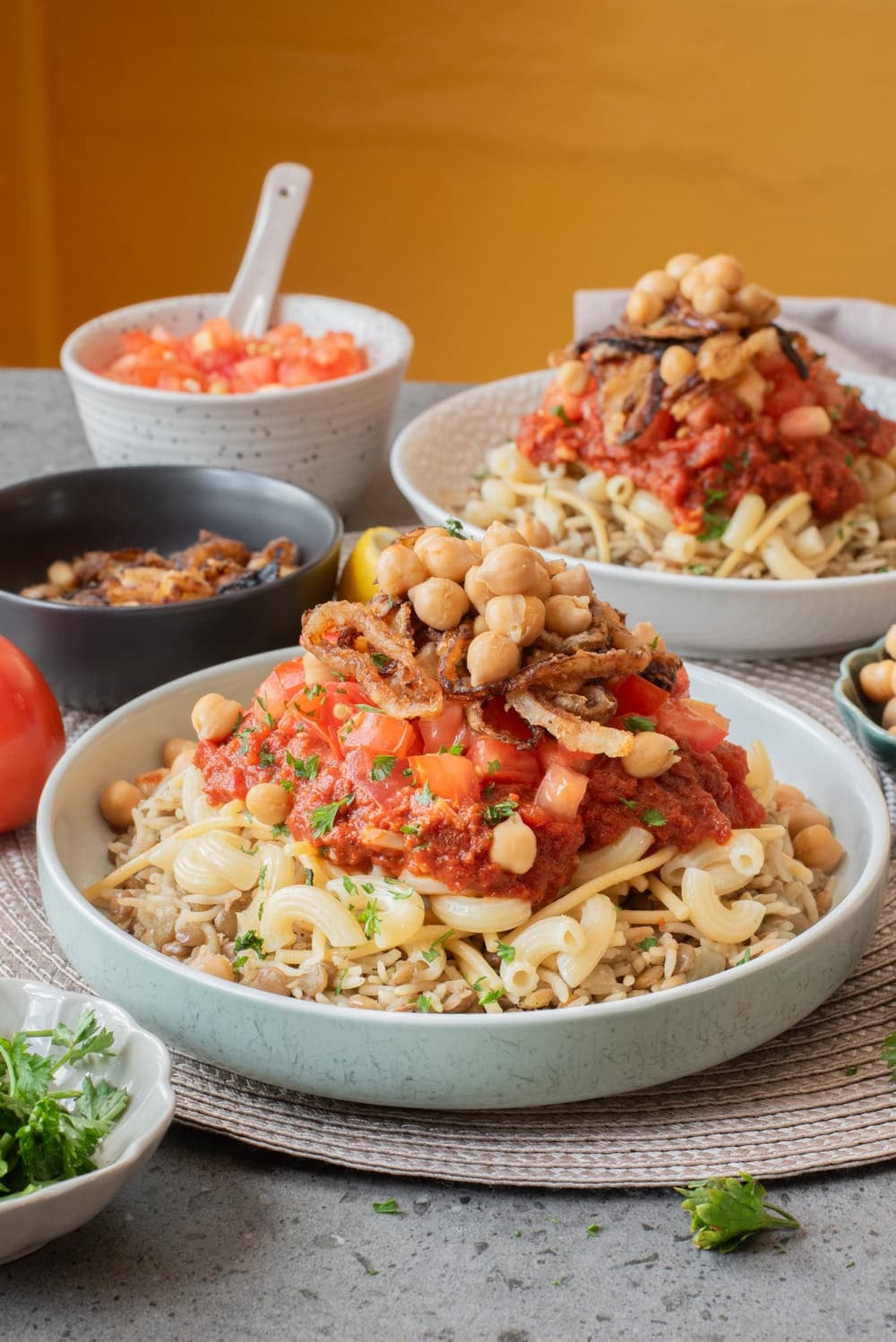 Bowl of Egyptian koshari topped with chickpeas, crispy onions, and two tomato sauces.