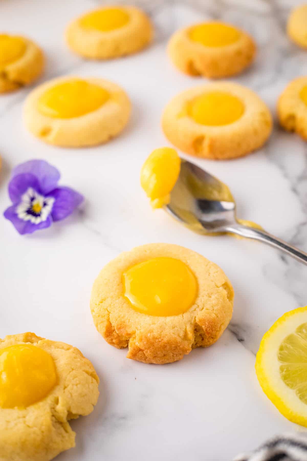 Close up of lemon curd cookie with spoonful of lemon curd and lavender flower in background.