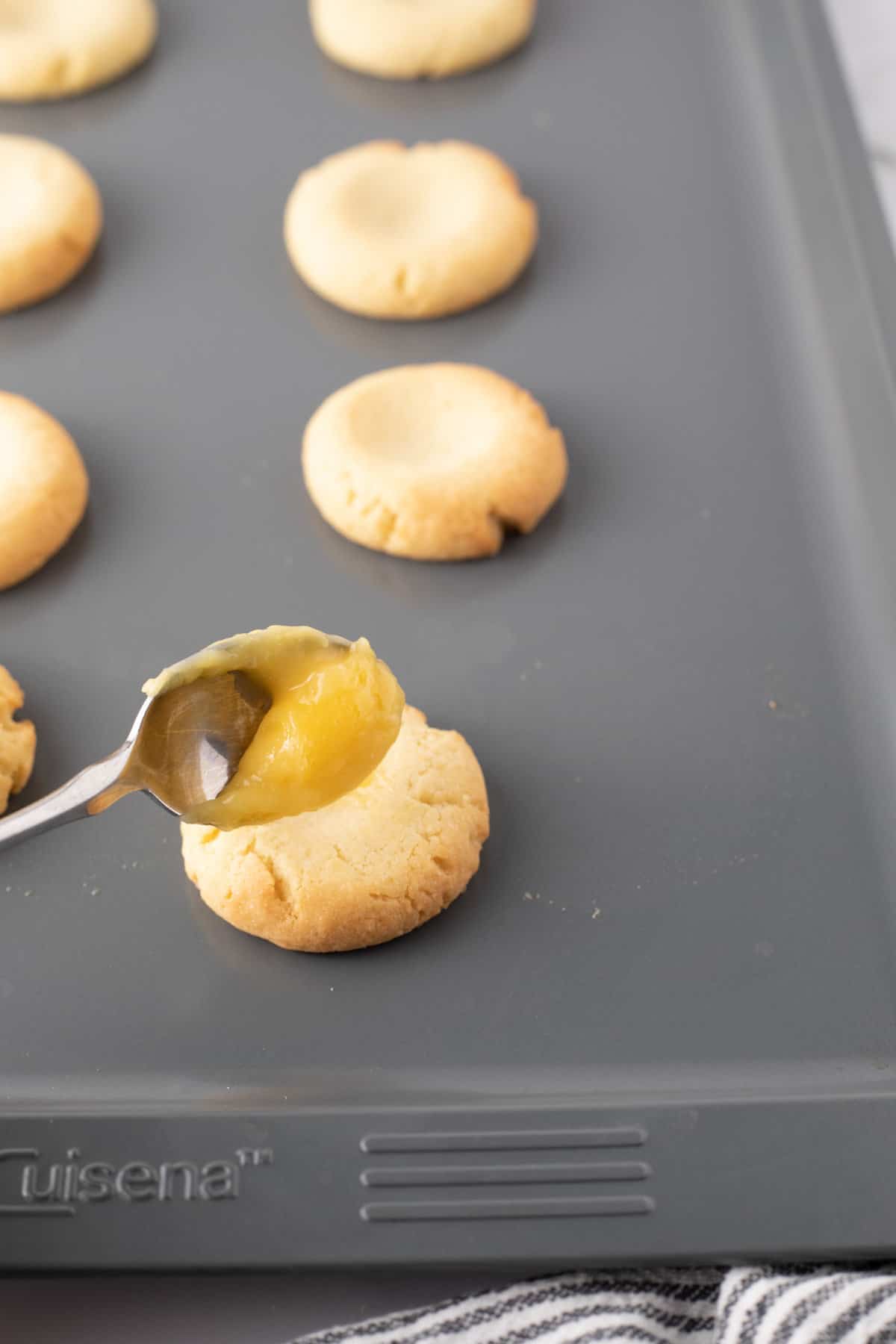 Side angle view showing spoon of lemon curd being added to cookies after being baked.