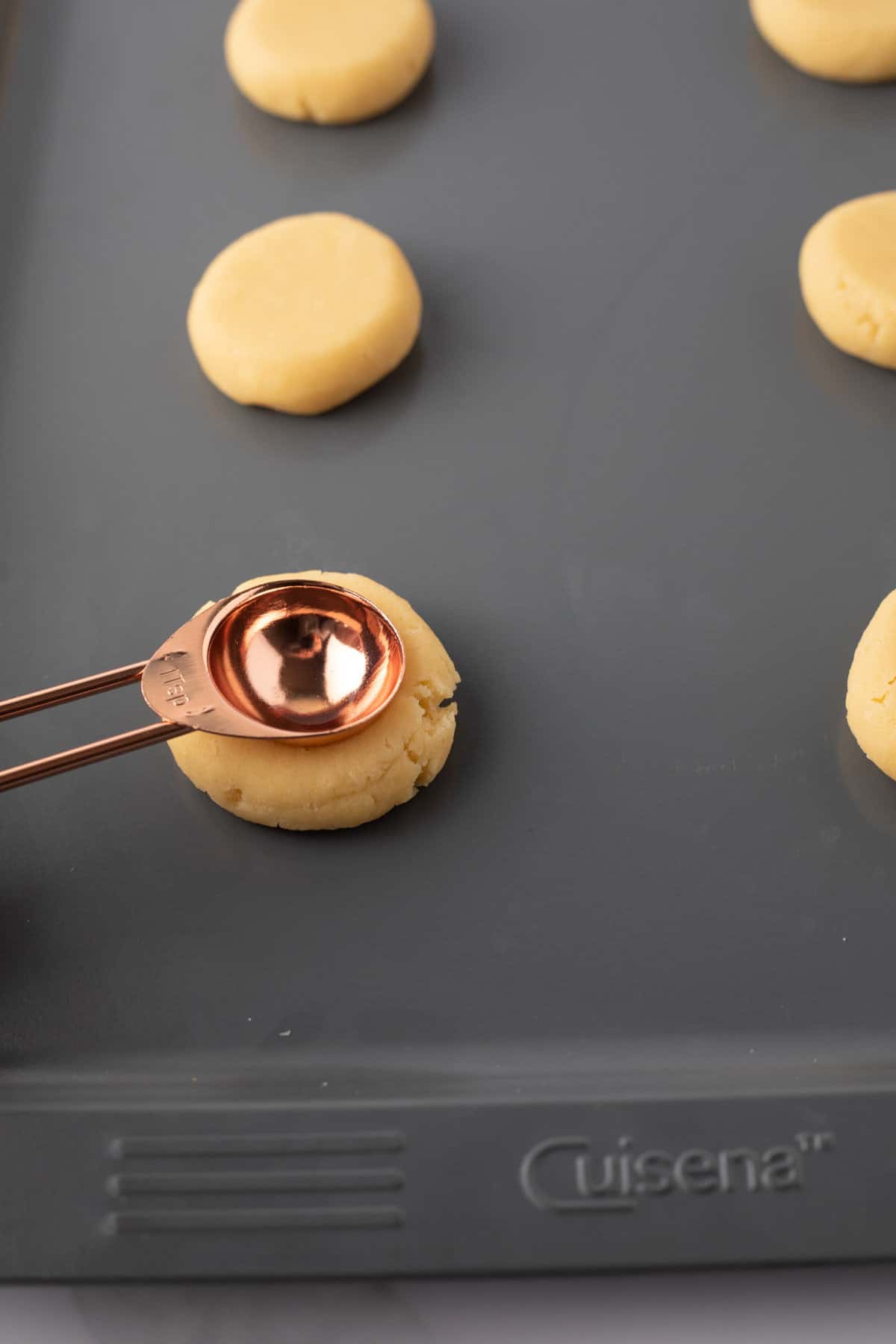 Side view showing how to press indent into flattened cookies using measuring spoon.
