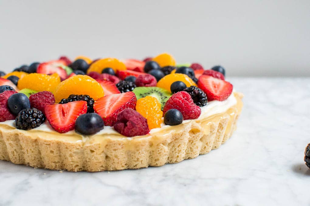 A straight view of a gluten-free fruit tart with lemon curd and cream cheese filling, with berries, oranges, and kiwi on top.