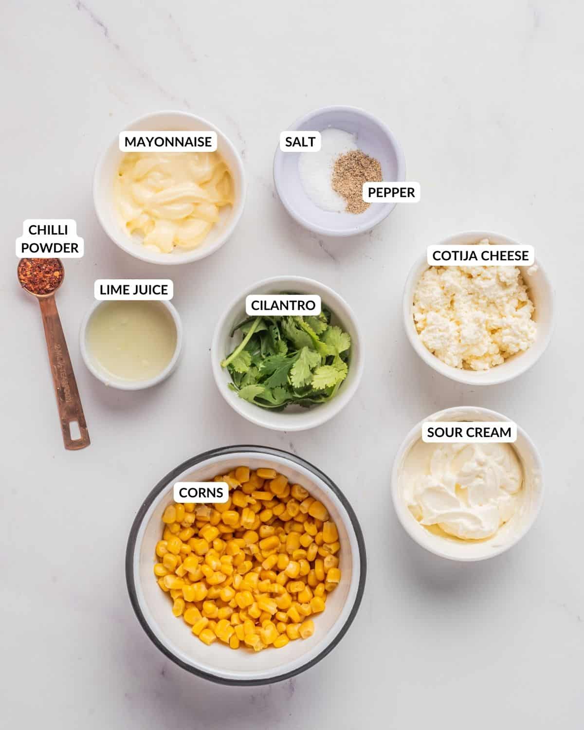 An overhead image of Mexican street corn salad ingredients in different containers with labels.