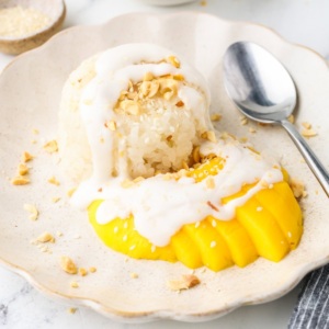 Close-up of mango sticky rice topped with coconut cream and crushed peanuts on a plate.
