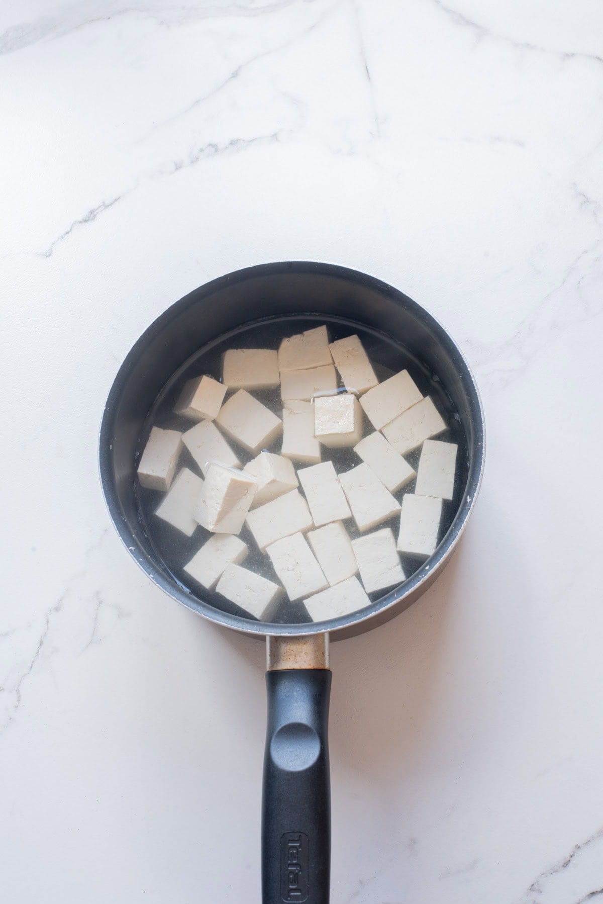 An overhead image of adding tofu cubes in a pot with water.