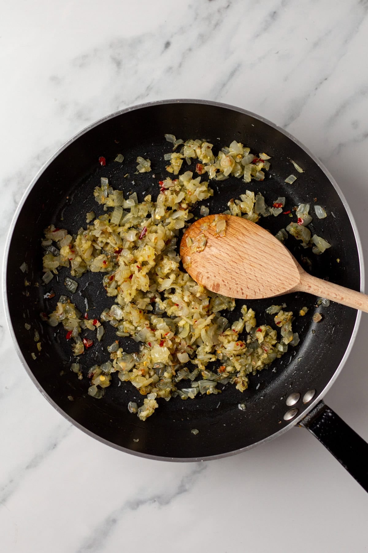 An overhead image of adding red chili flakes and garlic on a skillet.