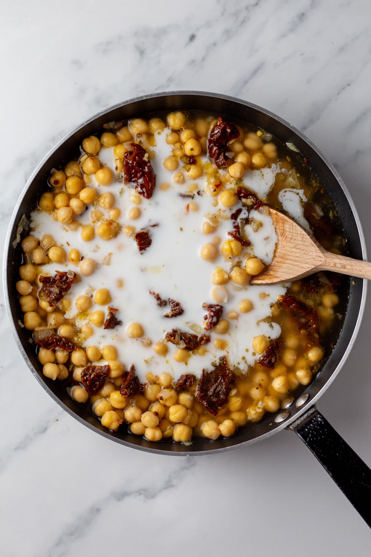 An overhead image of adding coconut milk to the mixture on a skillet.