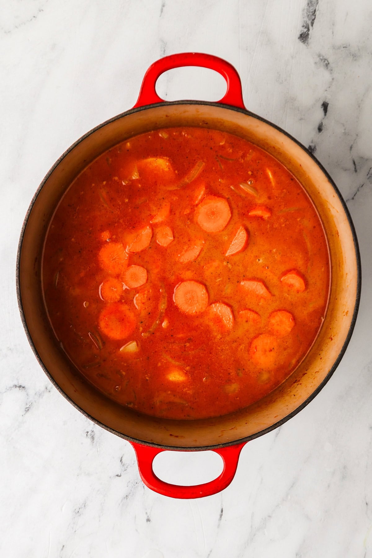 An overhead image of adding carrots and potatoes to the mixture.