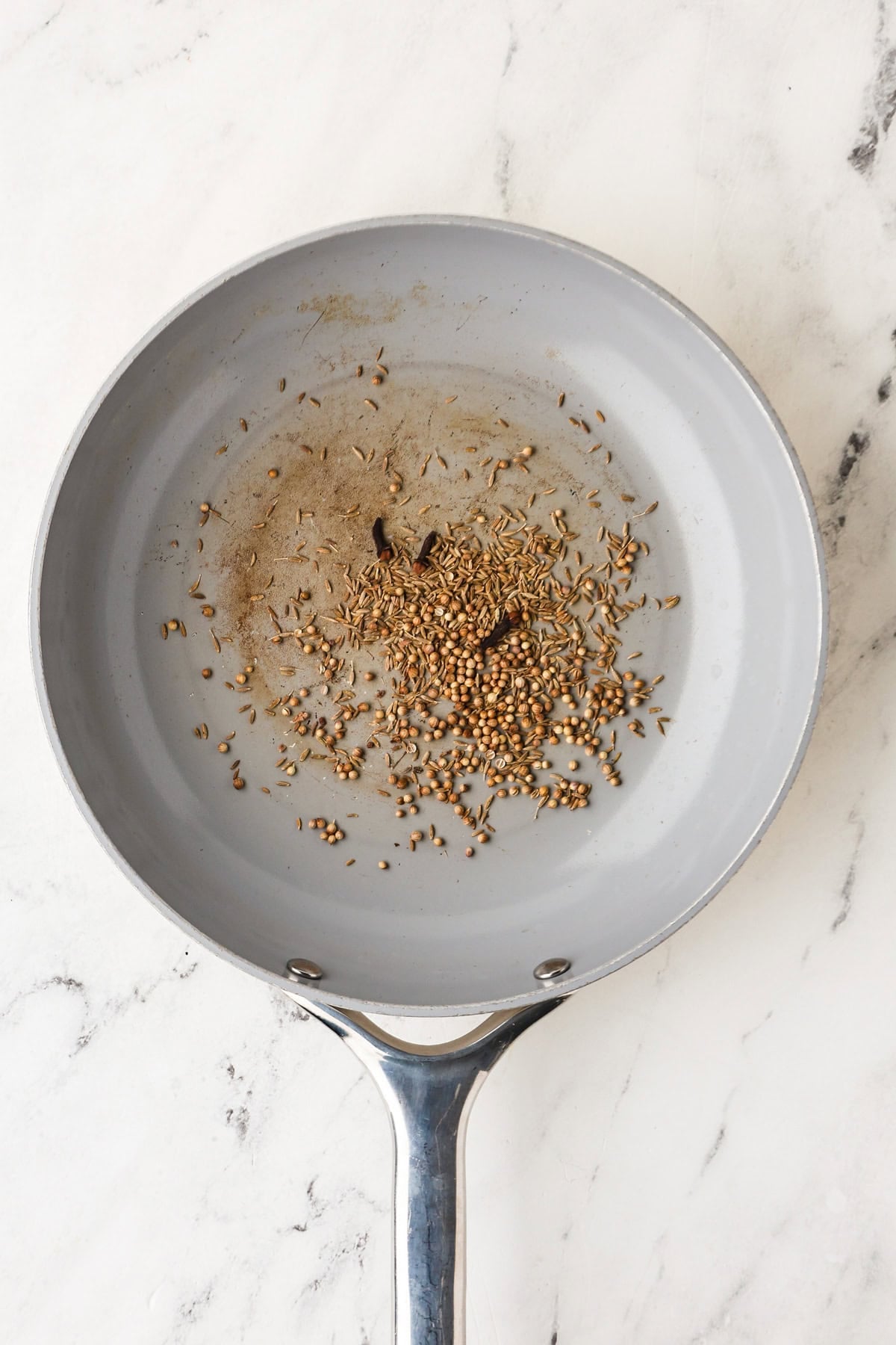Overhead image of the spices toasting in a skillet for massaman curry paste.
