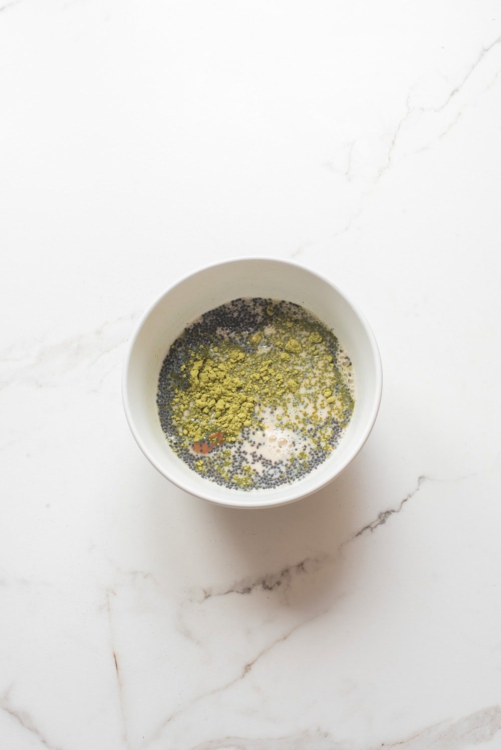 Overhead image of the ingredients of matcha chia overnight oats added in a bowl.