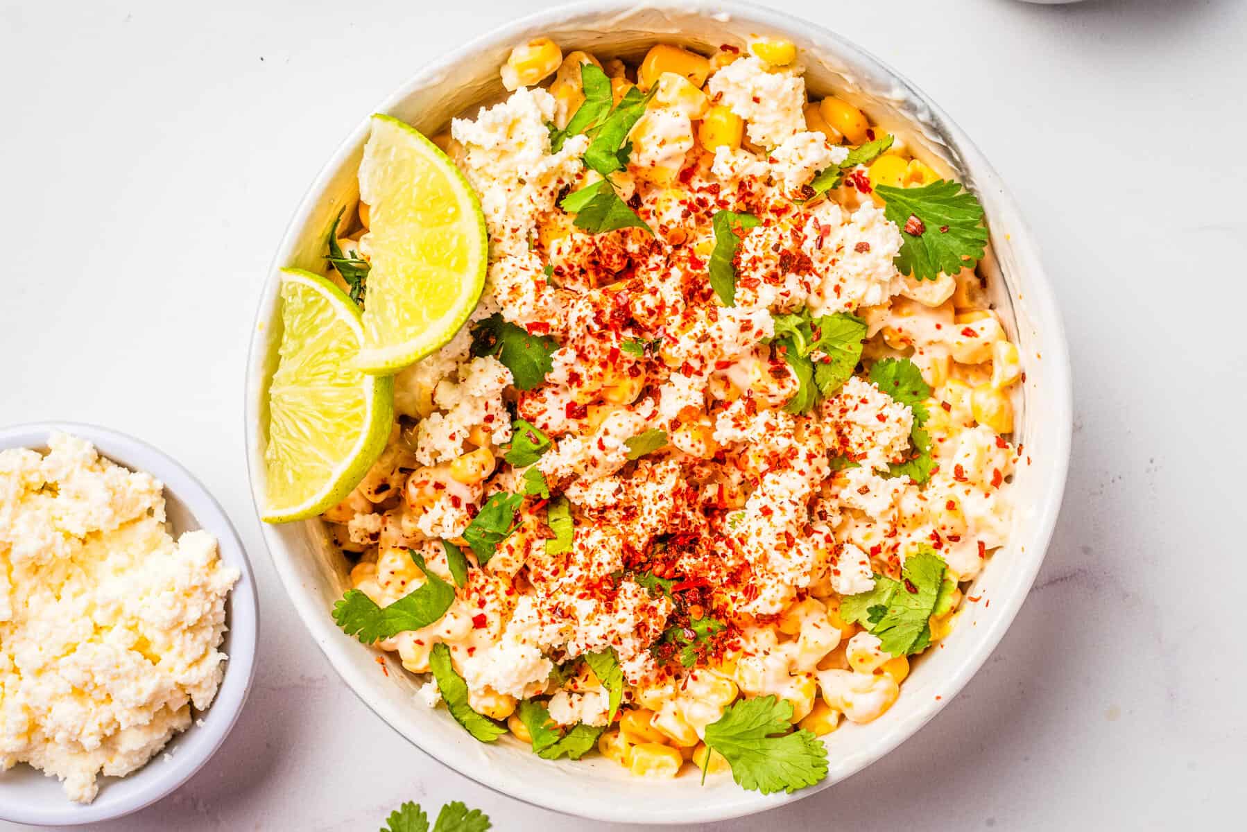 An overhead image of Mexican street corn salad in a bowl with two slices of lime resting on the side.