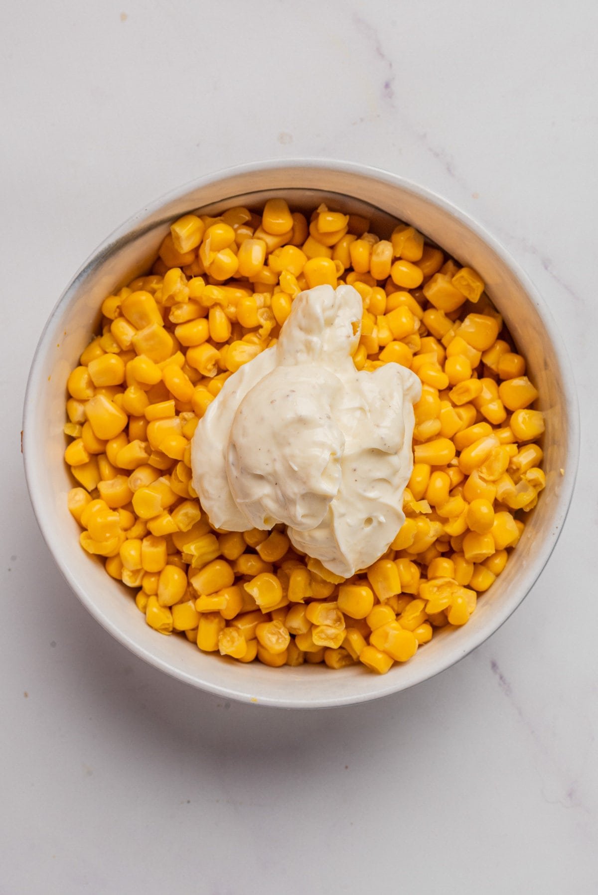 An overhead image of a bowl of corn kernels with the dressing on top, before mixing.