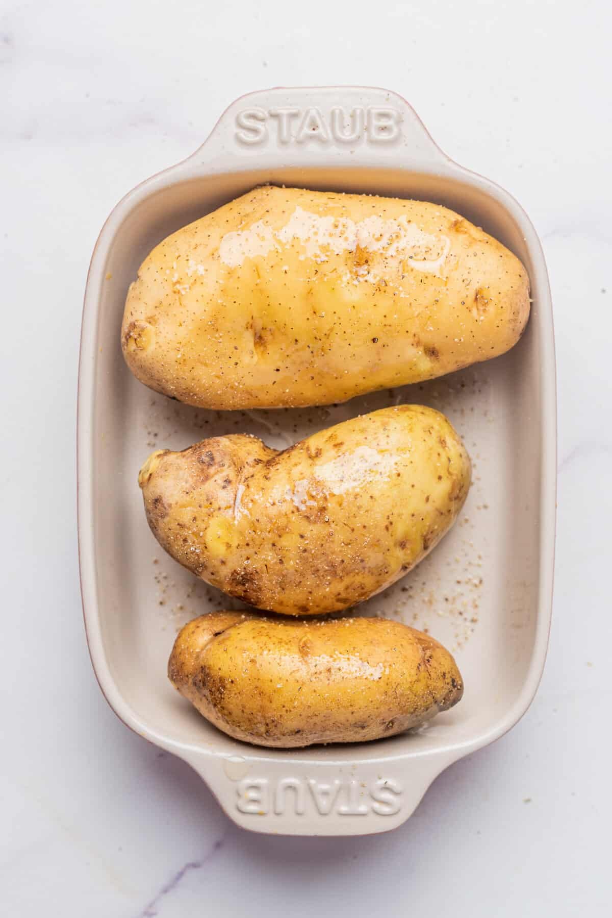 A photo of three potatoes in a microwave safe dish